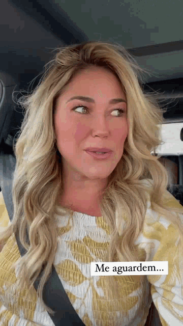 a woman wearing a yellow and white floral shirt is sitting in a car with a sticker that says me aguardem