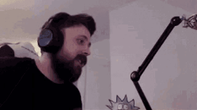 a man with a beard is wearing headphones and making a funny face in front of a microphone .