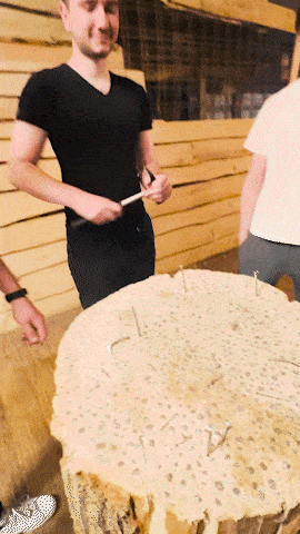 a man in a black shirt stands next to a large piece of wood with nails in it