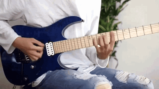 a person playing a blue electric guitar with a white shirt and ripped jeans
