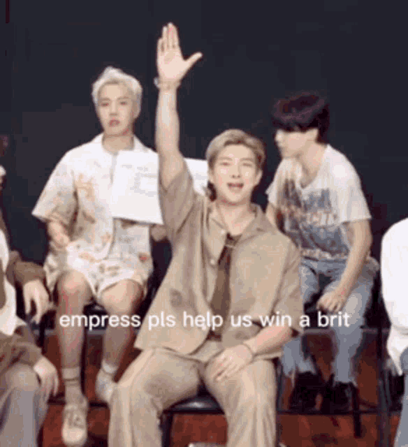 a man is sitting in a chair with his hand up and a caption that says empress pls help us win a brit