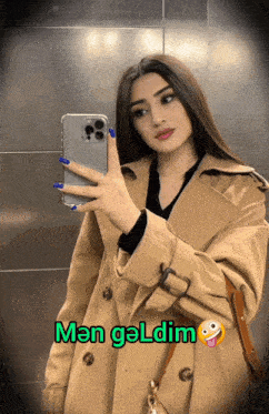 a woman in a trench coat is taking a picture of herself in a mirror with a caption that says " man geldim "