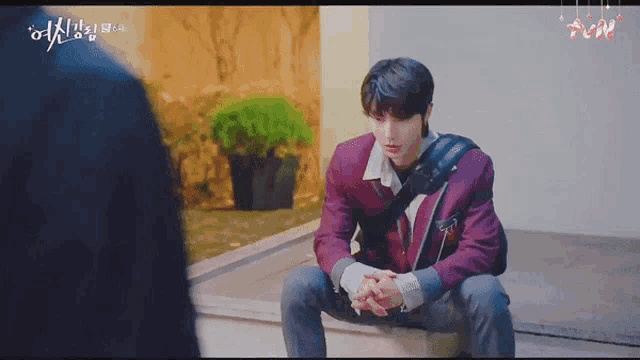 a young man in a red jacket is sitting on a bench with his hands folded