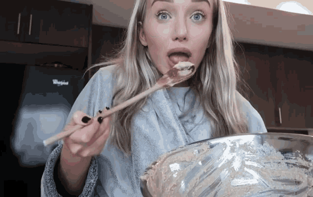 a whirlpool refrigerator is behind a woman holding a wooden spoon