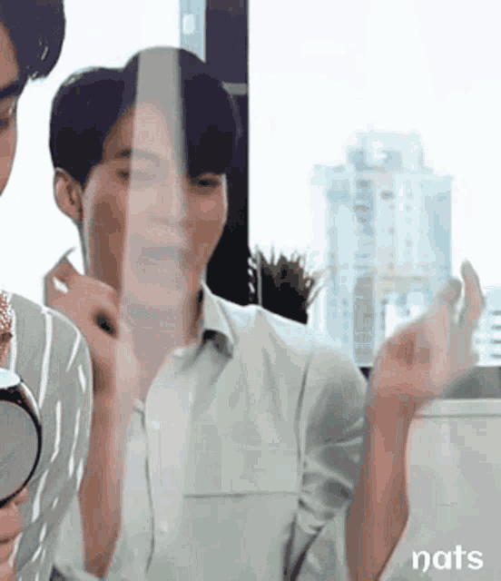 a man is looking at himself in a mirror while another man looks on .