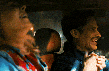 a man with a mustache is smiling while a woman laughs in the back seat of a car