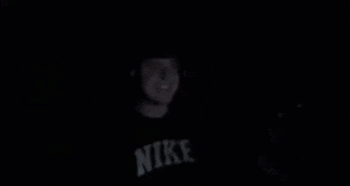 a man wearing a nike shirt is standing in the dark .