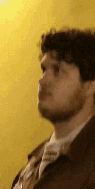 a man with a beard is wearing a brown jacket and a white shirt