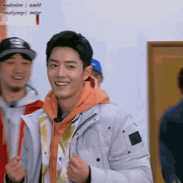a young man wearing a white jacket and an orange hoodie smiles