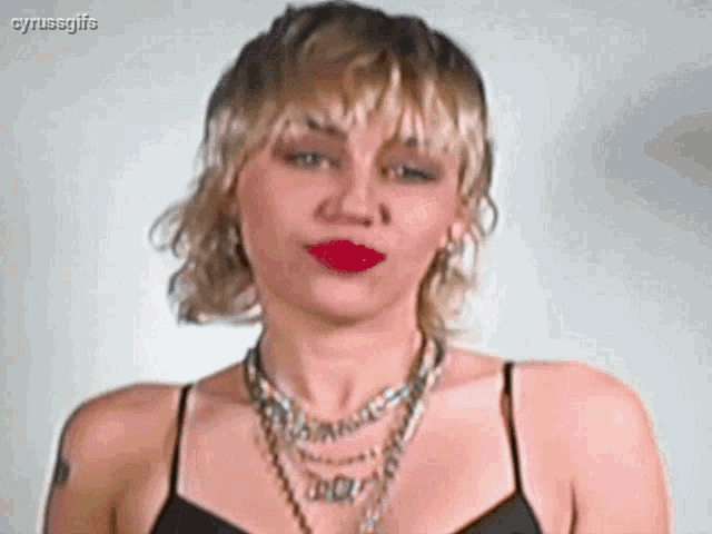a woman with blonde hair and red lipstick is wearing a black top and a necklace .