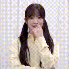 a woman in a yellow shirt is covering her mouth with her hand and smiling .