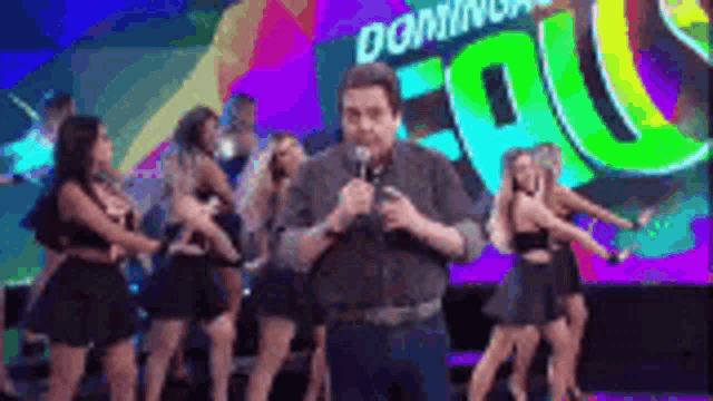 a man is standing on a stage with a microphone in front of a group of dancers .