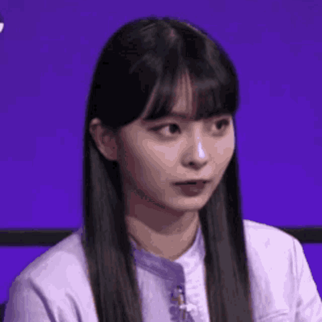 a young woman with long black hair and bangs is sitting in front of a purple background .