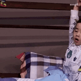a young boy is laying on a bed with his arms up