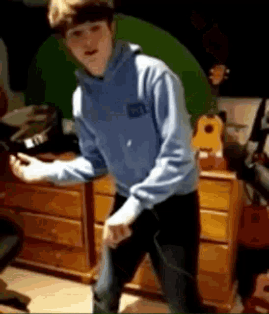 a boy in a blue hoodie is dancing in a room