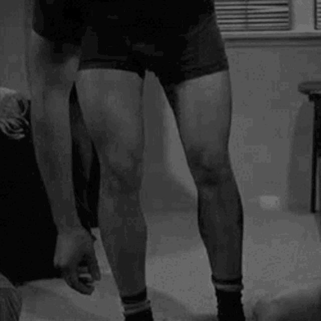 a man in boxer shorts and socks is standing in a room in front of a window .