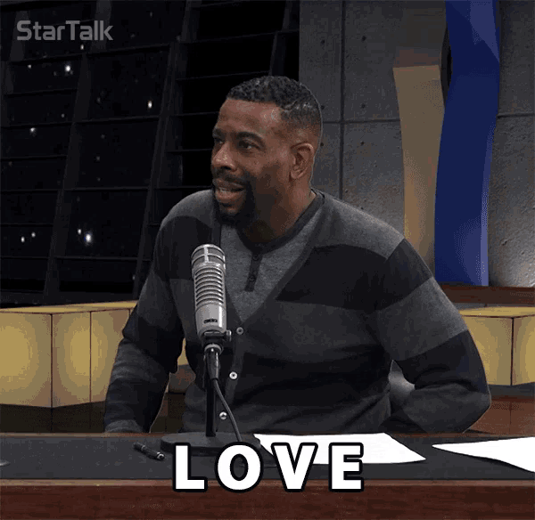 a man sitting at a desk with a microphone and the word love written on it