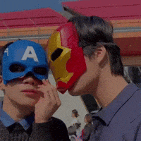 a man wearing an iron man mask kisses another man wearing a blue captain america mask