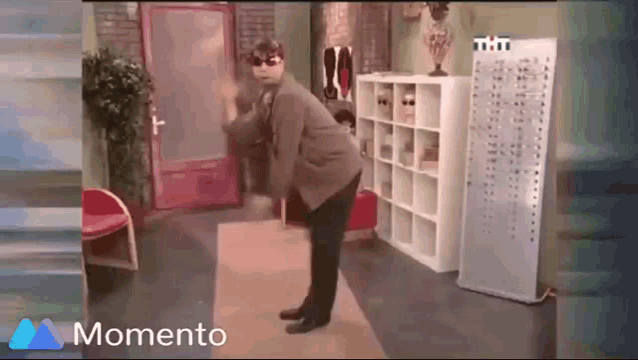 a man in a suit and sunglasses is dancing in a room with a momento logo in the corner