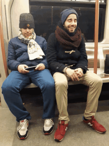 a man wearing a scarf is sitting next to another man on a train