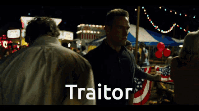 a man stands in front of a carnival booth that says " traitor "