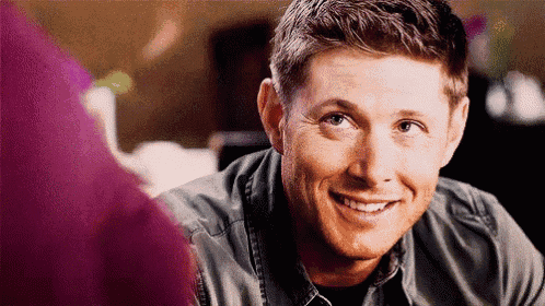 a man in a denim shirt is smiling and looking at the camera while sitting at a table .