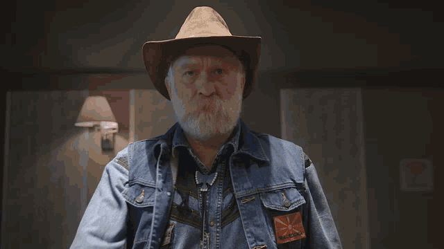 a man with a beard wearing a cowboy hat and a blue jacket