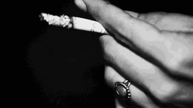 a black and white photo of a person smoking a cigarette with a ring on their finger .
