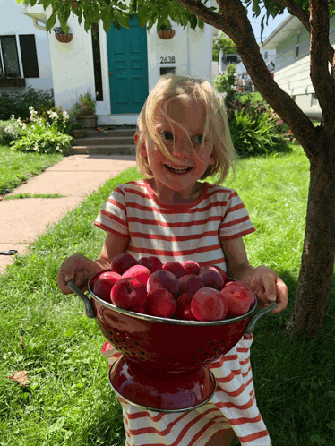 a little girl is holding a bowl of apples in front of a house with the number 2638 on it