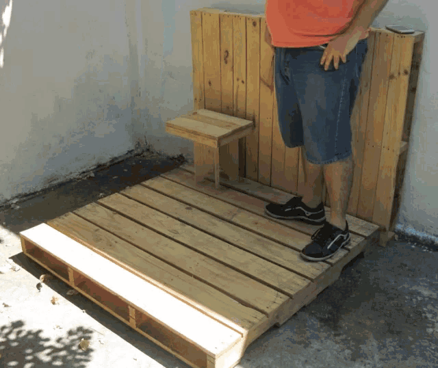 a man standing on a wooden pallet with a stool on it