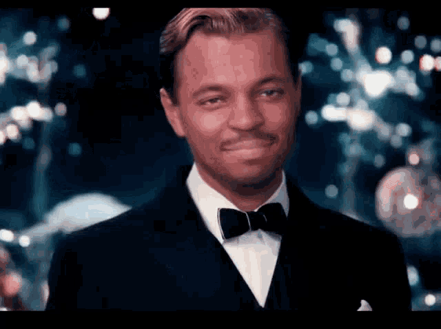 a man in a tuxedo and bow tie is smiling and looking at the camera