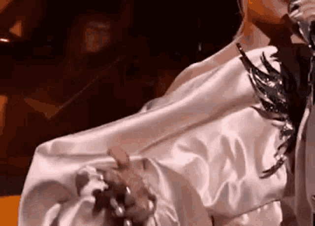 a woman is singing into a microphone while wearing a white satin shirt with feathers on it .