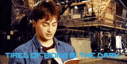 a man is reading a book with the words " tired of being in the dark " written above him