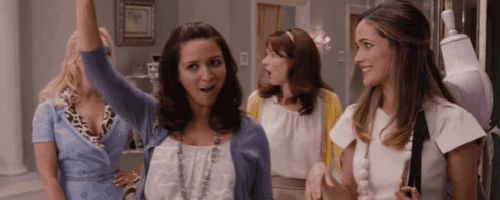 a group of women are standing in a room and one woman is raising her hand