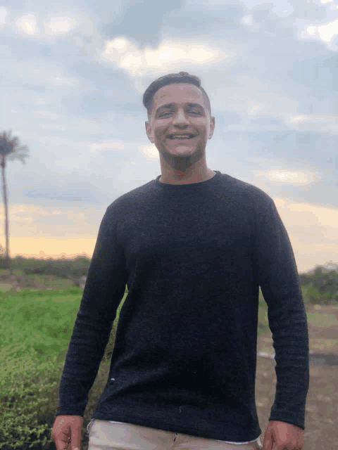 a man in a black sweater is smiling in front of a cloudy sky