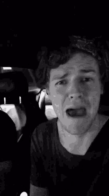 a black and white photo of a young man making a funny face in a car .