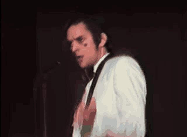 a man in a white shirt is singing into a microphone in a dark room