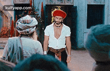 a man in a white shirt and a red hat is standing in front of a group of people .