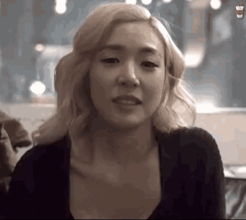 a woman with blonde hair is wearing a black shirt and making a face .
