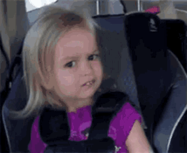 a little girl is sitting in a car seat wearing a seat belt .