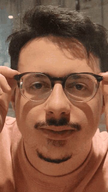 a man wearing glasses and a pink sweater looks at the camera