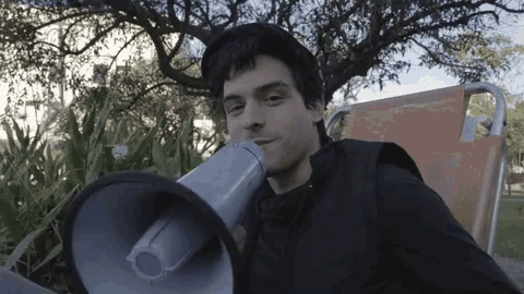 a man is holding a megaphone in his mouth while sitting in a chair