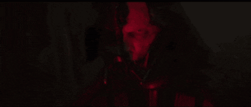 a close up of a person 's face in a dark room with a red light behind them .