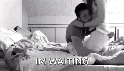a man and woman are kissing on a bed with the words `` im waiting '' written on the bottom .