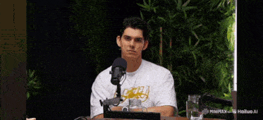 a young man is sitting at a table in front of a microphone and talking into it .