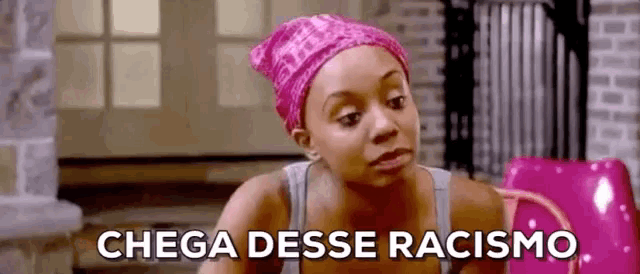 a woman wearing a pink head scarf is sitting in front of a pink chair and says chega esse racismo .