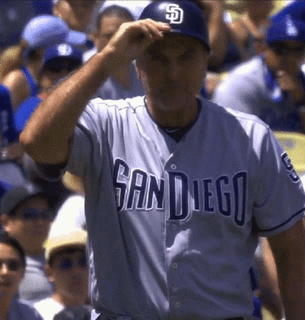 a man wearing a san diego baseball jersey adjusts his hat
