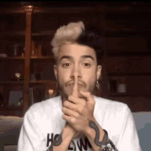 a man with a snake tattoo on his arm is holding his finger to his mouth .