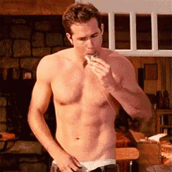 a shirtless man is eating a piece of food while standing in a room .
