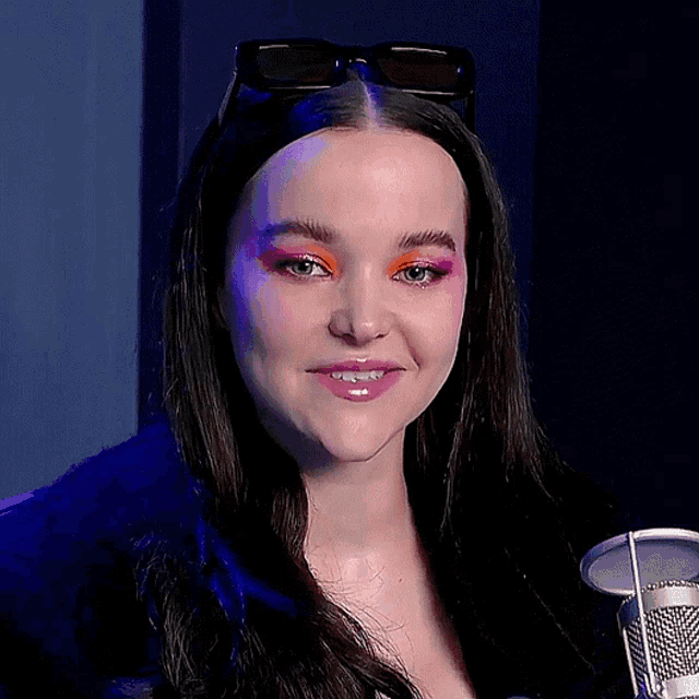 a woman wearing sunglasses is smiling and holding a microphone